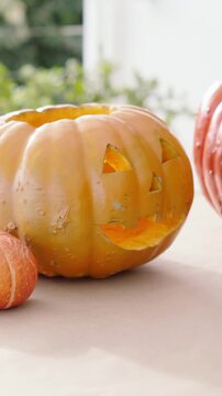 Vertical video: Panning cam framing carved jack o lantern on table by window, showing mini pumpkin