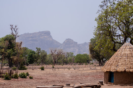 View of a traditional thatched-roof hut in a dry, arid landscape with rocky hills in the background in Bauchi, Bauchi, Nigeria.