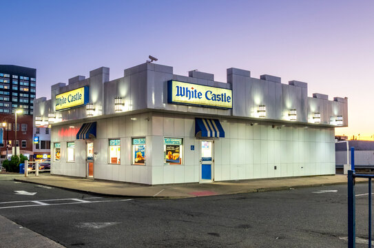 Jersey City, NJ - US - Oct 7, 2026 : A White Castle restaurant in Jersey City stands illuminated at dusk, with castle-inspired parapets, blue striped awnings, glowing signs and a paved parking area