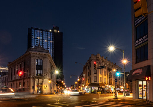 Jersey City, NJ - US - Oct 7, 2026 : Traffic crosses Five Corners at Newark, Summit and Hoboken avenues at dusk, past the historic Jersey City Trust Company building, shops and glowing streetlights