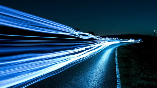 Long exposure photograph of bright blue light trails on a dark, wet, winding road at night