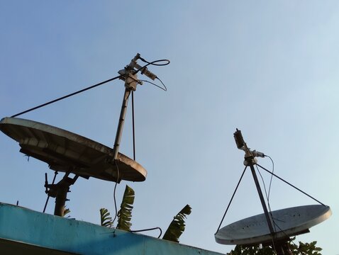 Two parabolic satellite dish antennas mounted side-by-side on rooftop under clear blue sky.