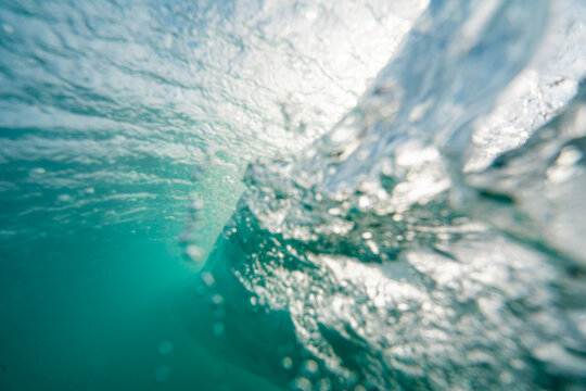 View of a breaking wave underwater with clear turquoise water, light refraction, and bubbles, Newquay, England, United Kingdom.