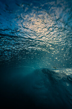 View of a breaking wave captured from underwater with sunlight filtering through the turbulent surface in Newquay, England, United Kingdom.