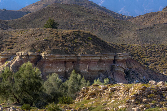 View of the rugged landscape and layered rock formations of the Sulaiman Mountains with sparse desert vegetation under a clear sky in Dera Ghazi Khan, Punjab, Pakistan.