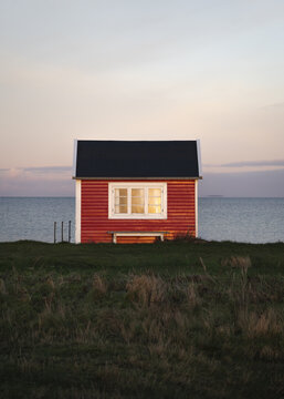 View of a traditional red wooden beach house at sunrise with calm sea in the background in Aero Municipality, Denmark.