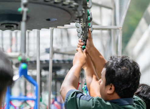 Close-up of a mechanic's hands inspecting overhead track components and gear linkages in a modern facility.