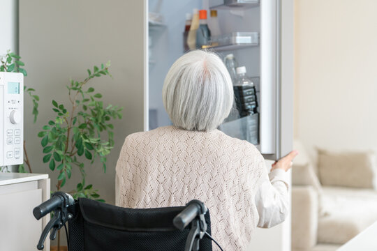 A senior woman in a wheelchair opening the refrigerator and looking for ingredients. An image of independent daily living and household chores