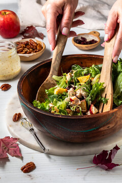 Hands using wooden salad tongs to toss a homemade Fall Harvest Salad