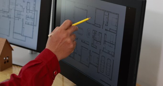 Architect points with a pencil at a digital house floor plan on a computer screen beside a small wooden model.