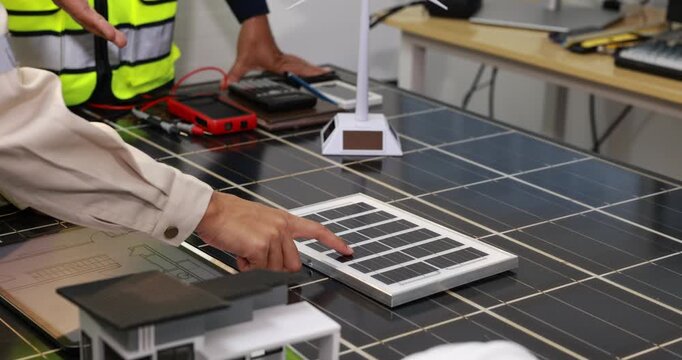 Technicians test a solar panel system on a workbench, using a digital meter and portable solar module in a renewable energy workshop.