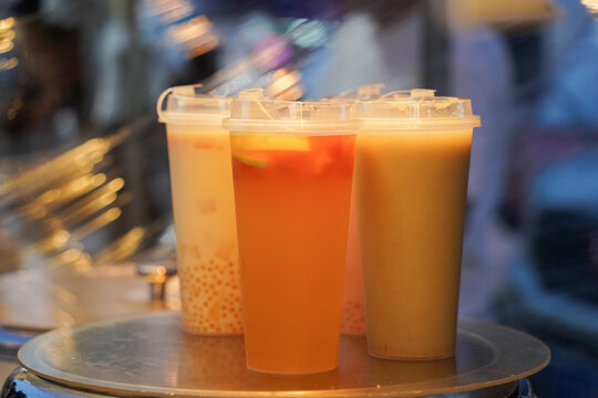 Four plastic cups of bubble tea, one white and one orange in night market