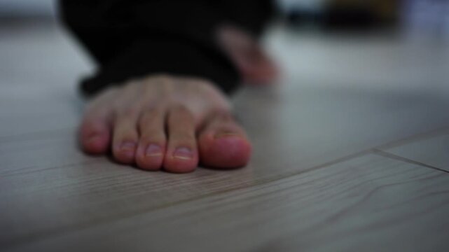 室内のフローリングを裸足で歩く男性の足元クローズアップ