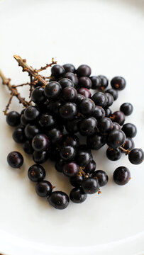 A cluster of ripe Euterpe oleracea berries resting on a smooth white surface, highlighting their round shape and rich color, conveying a sense of vitality and wellness
