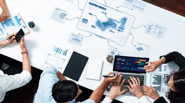 A diverse team collaborates around a modern office table, analyzing electric vehicle data with laptops and charts, showcasing teamwork and innovation in technology and design. Raster