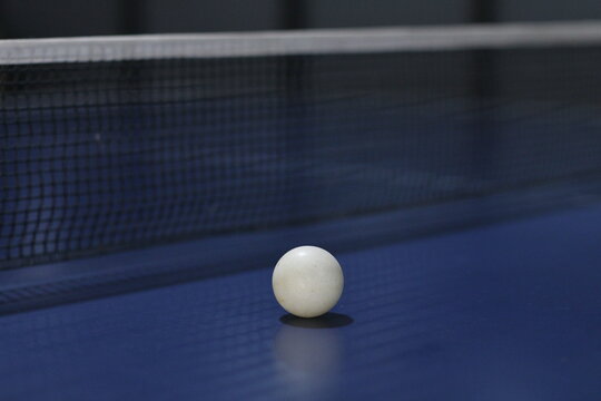 Table tennis racket and white ball on a blue ping pong table near the net