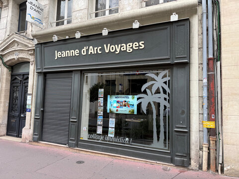 Exterior of Jeanne d'Arc Voyages travel agency with a lowered roller shutter, travel advertisements and palm tree graphics on the display window - Rouen, France - September 6, 2026