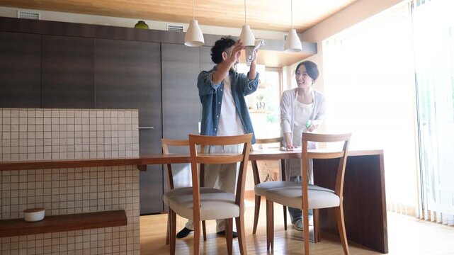 自宅のダイニングで大掃除や家事を協力して行う日本人夫婦、共働き家庭の家事分担と家事シェア、テーブルや窓の拭き掃除をする男女の快適なライフスタイルイメージの動画