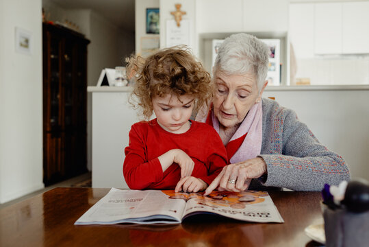 Happy Grandmother reading a magazine with her young 4 year old grandson sitting on her lap at home; Melbourne, Victoria, Australia.