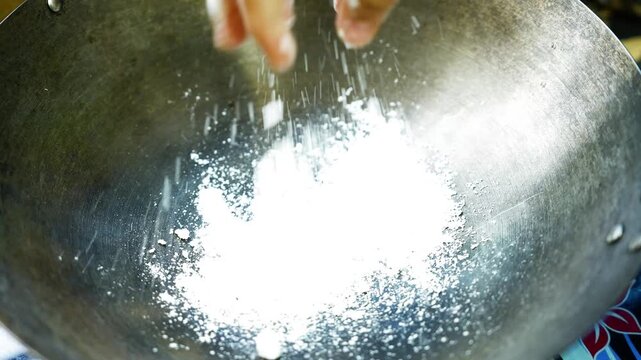 Worn metal wok with bright reflections and residue, Close-up view of a worn silver metal wok with white powder-like residue, curved interior, scratches, and bright reflections