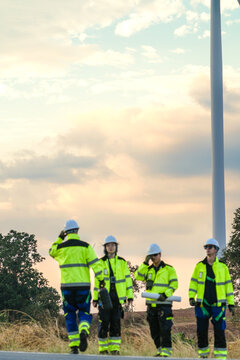 Vertical image of The wind farm crew of four close the day with a roadside debrief on the park road under fading skies in pink pastel dusk at a utility scale wind power project.