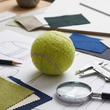 Yellow Tennis Ball on Product Design Sketch with Fabric Samples and Measuring Tools