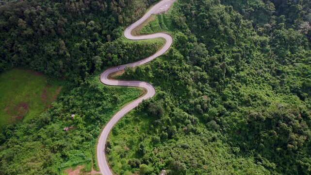 Top view of countryside road passing through the green forrest and mountain