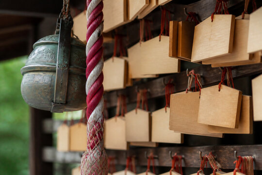Wooden ema prayer plaques hanging at a Japanese shrine beside a bell rope