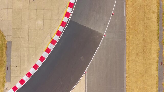 A high speed race car navigates a sharp curve on an asphalt racing circuit surrounded by dry yellow grass during a sunny afternoon while racing on the track surface.