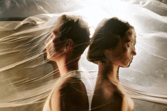 Young adult Caucasian man and woman standing back to back covered by transparent plastic film, symbolizing suffocation and relationship crisis, suitable for mental wellbeing campaigns