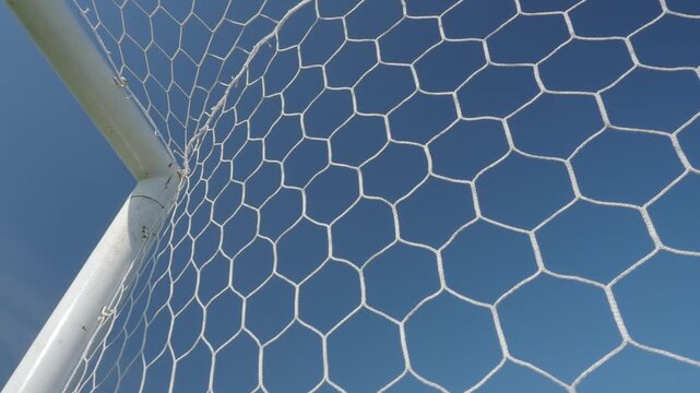 White synthetic football goal net with a hexagonal mesh pattern stands out against the azure sky.