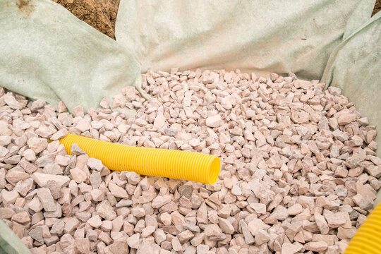 From a top view, a yellow drainage pipe is placed amidst small gravel stones in a construction area.