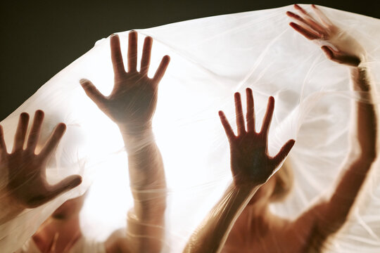 Caucasian young adults pressing hands against plastic film representing suffocation, confinement, and anxiety. Concept for mental health awareness campaigns and editorial storytelling