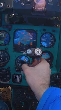 Hand operates flight controls inside military helicopter cockpit, instruments show altitude and speed, teal dashboard with Cyrillic text, red and blue lighting, focused on pilot interaction