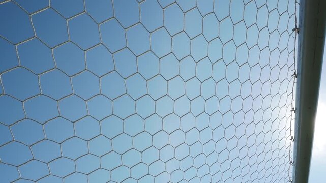 White synthetic football goal net with a hexagonal mesh pattern stands out against the azure sky.
