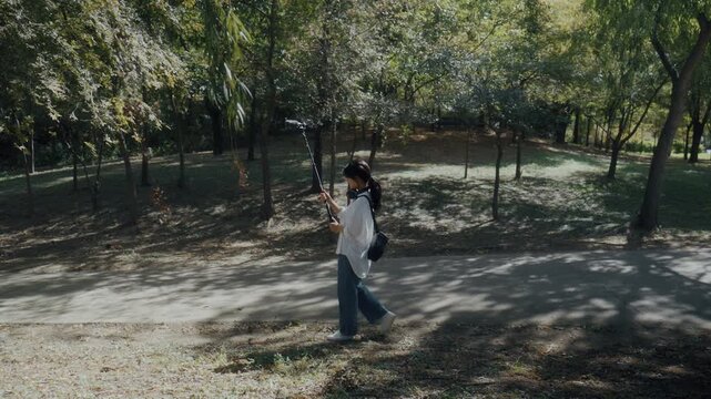 Young Asian Woman Holding Boom Microphone Up to Tree Leaves to Record Nature Sounds in Park