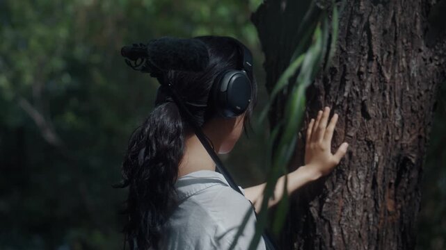 Young Asian Woman Touching Tree Bark and Recording Nature Sounds with Boom Microphone in Forest