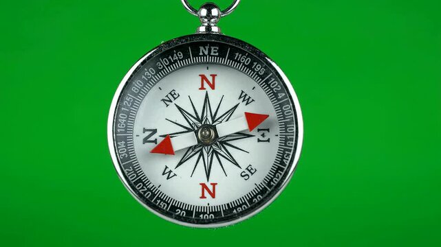 Silver compass spinning needle against solid green chroma key backgrou