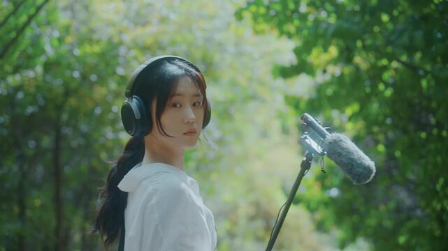 Young Asian Woman with Headphones and Boom Microphone Turning Around and Looking at Camera in Park