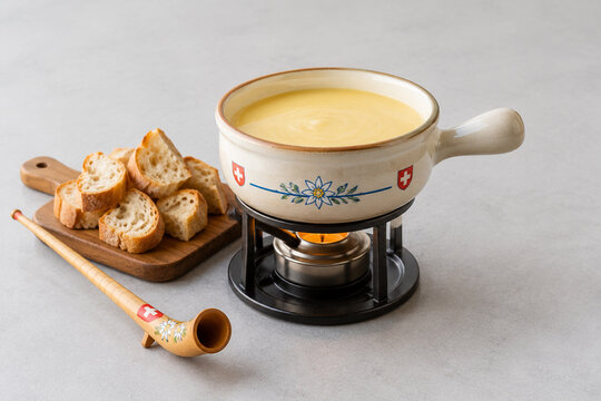 Ceramic cheese fondue pot with melted cheese, bread and carved alphorn, cozy dining concept