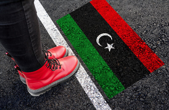 a woman with a boots standing on asphalt next to flag of Libya and border
