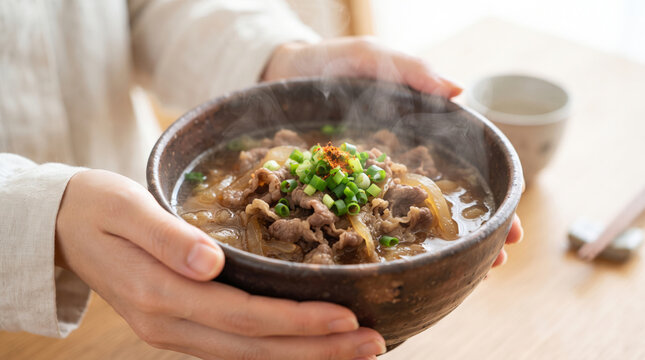 温かい肉うどんを持って食べる女性の手元