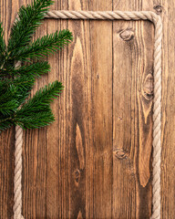 Rustic Christmas background with evergreen fir branches and natural jute rope forming a decorative border on wooden planks. Vertical holiday frame with generous copy space for Christmas greetings © hannamartysheva