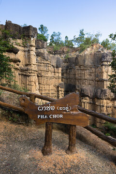 Rustic wooden PHA CHOR sign with Thai lettering stands beside log railing overlooking eroded cliffs at Pha Chor, Mae Wang National Park, Doi Lo, Chiang Mai, Thailand. Vertical travel view of canyon.