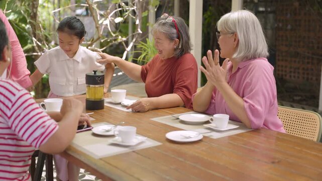 Retired women turn toward their arriving friend while gathering around outdoor cafe table, celebrating friendship, quality time, social connection through retirement lifestyle outdoors.