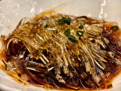 sliced translucent fish maw jelly in sauce, garnished with chopped scallions.