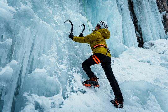 Ice climber with ice axes ascending a frozen blue waterfall, Almaty, Kazakhstan