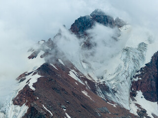 Snow-capped rocky mountain peak wrapped in drifting clouds, aerial view, Almaty, Kazakhstan © mdpsycho