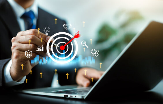 Business person working on a laptop with a target dartboard and growth icons interface. Concept of corporate strategic planning, goal achievement, business success, and financial target management.