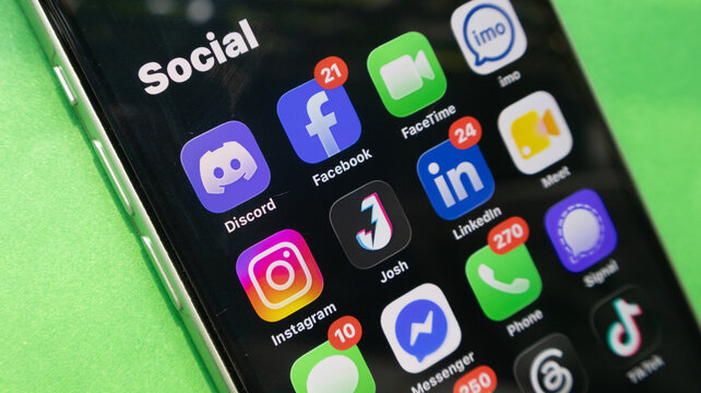A close up view of the black screen of an iphone showing social media apps on a green background.